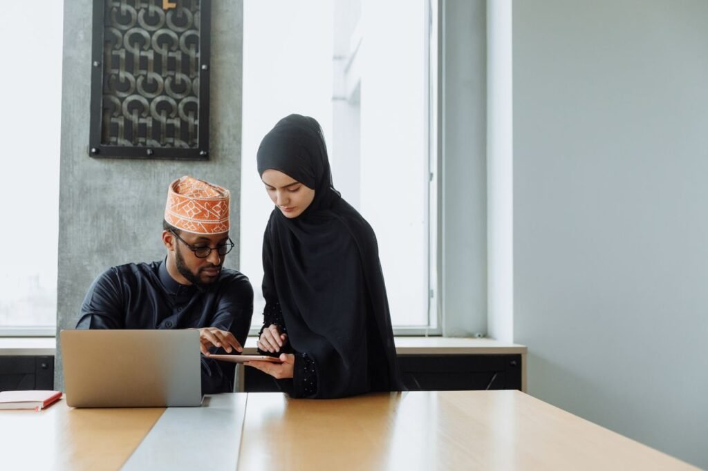 Muslim man and woman collaborate using a laptop and tablet in a modern office setting.